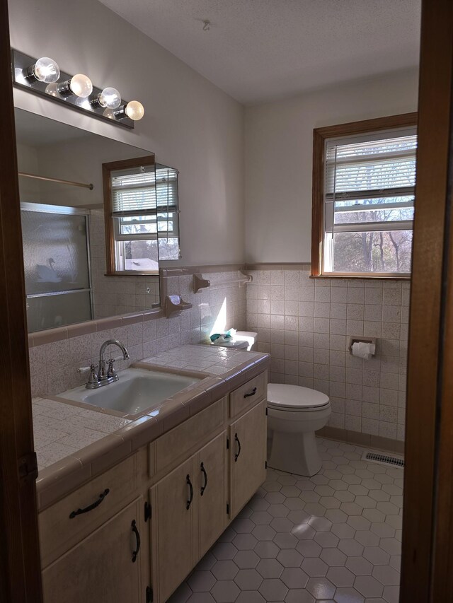 bathroom featuring vanity, a shower, tile patterned flooring, toilet, and tile walls