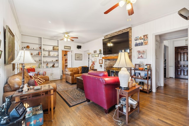 living room featuring built in shelves, hardwood / wood-style flooring, a brick fireplace, and crown molding