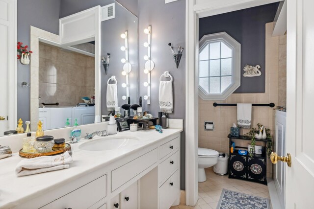 bathroom featuring tile patterned floors, vanity, tile walls, washer / clothes dryer, and toilet