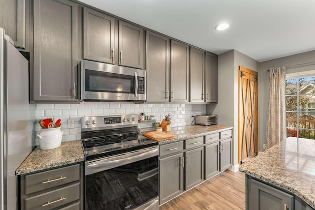 kitchen with backsplash, light stone countertops, light wood-type flooring, and appliances with stainless steel finishes