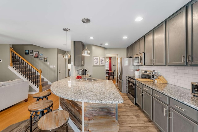 kitchen with pendant lighting, sink, light hardwood / wood-style flooring, light stone countertops, and appliances with stainless steel finishes