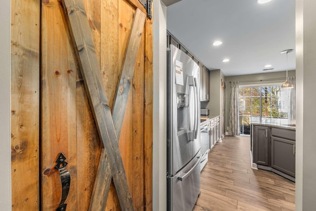 kitchen with light stone counters, stainless steel appliances, a barn door, light hardwood / wood-style floors, and hanging light fixtures