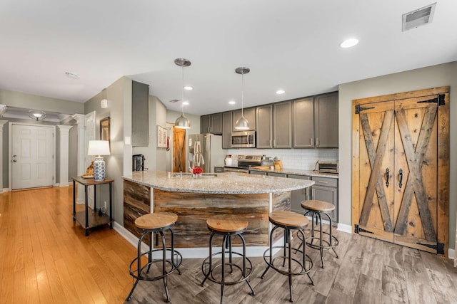 kitchen with hanging light fixtures, light hardwood / wood-style flooring, gray cabinets, light stone countertops, and stainless steel appliances