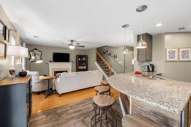 kitchen with a tile fireplace, ceiling fan, sink, gray cabinets, and light wood-type flooring