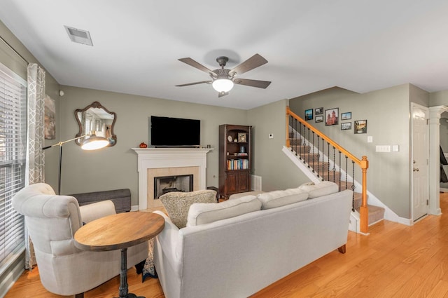 living room featuring a tiled fireplace, ceiling fan, and light hardwood / wood-style flooring