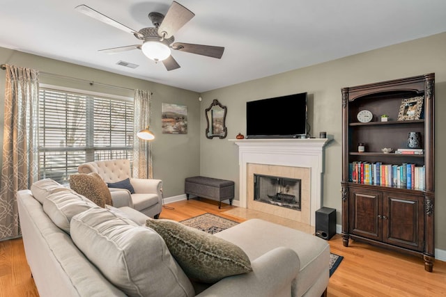 living room featuring a tile fireplace, ceiling fan, and light wood-type flooring