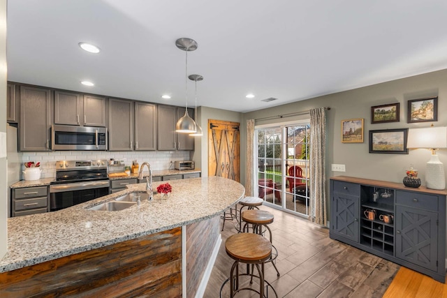 kitchen featuring appliances with stainless steel finishes, light stone counters, sink, light hardwood / wood-style flooring, and hanging light fixtures