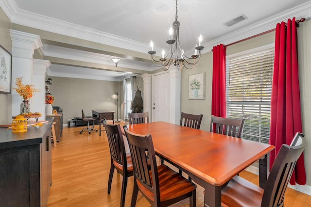 dining space featuring light hardwood / wood-style floors, an inviting chandelier, crown molding, and ornate columns