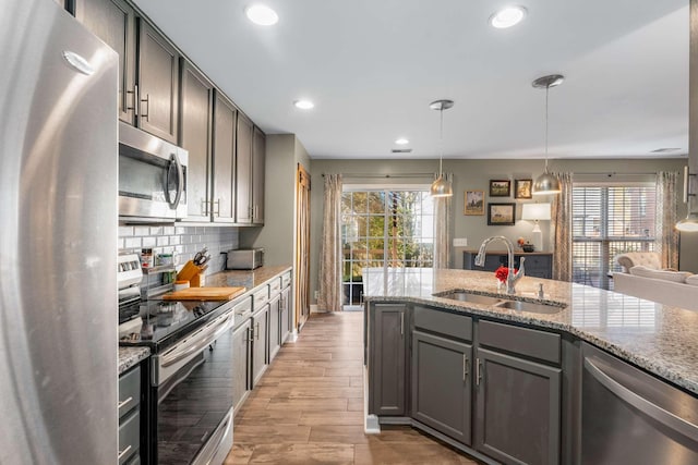 kitchen with light stone counters, sink, light wood-type flooring, and appliances with stainless steel finishes