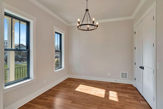 empty room featuring crown molding, a healthy amount of sunlight, wood-type flooring, and an inviting chandelier