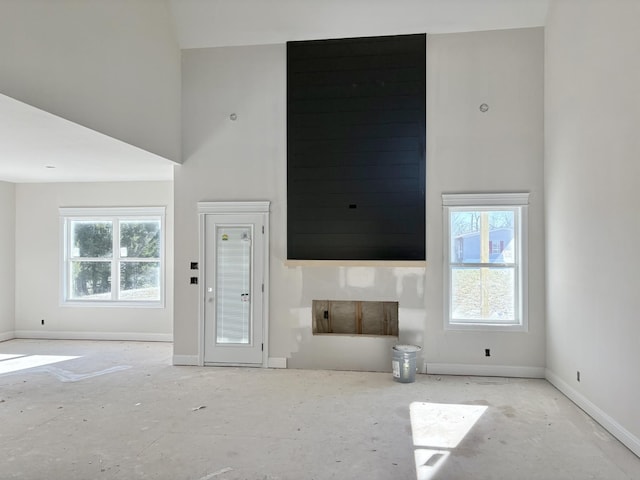 unfurnished living room with a towering ceiling, plenty of natural light, and baseboards