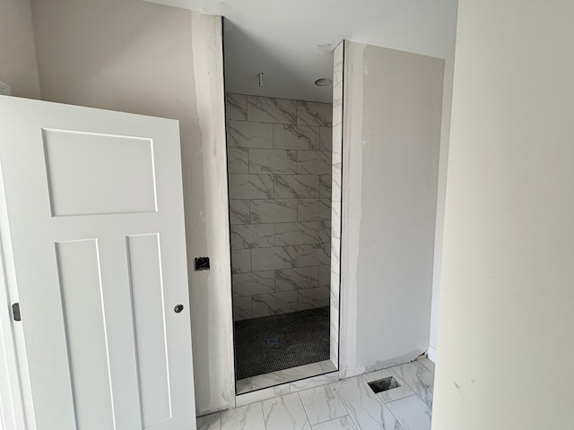 bathroom with marble finish floor and a tile shower