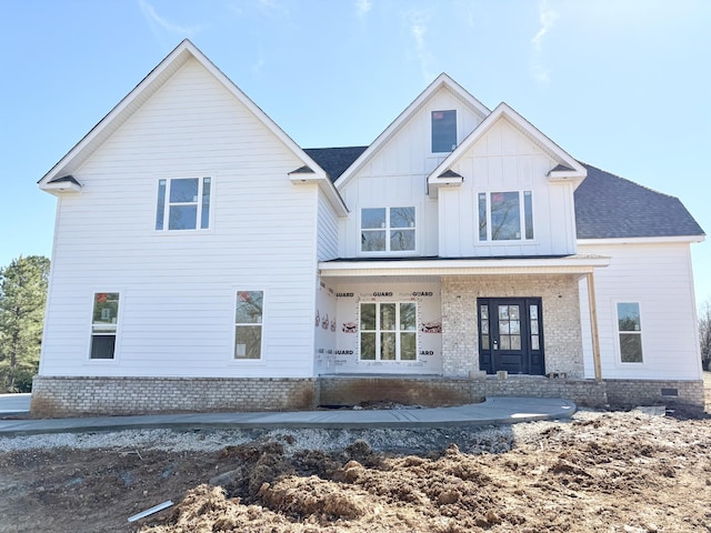 view of front of home featuring board and batten siding, brick siding, a porch, and roof with shingles