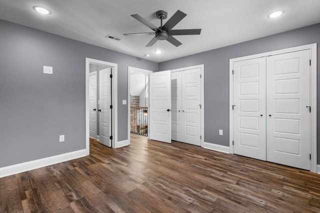 unfurnished bedroom with ceiling fan, dark hardwood / wood-style flooring, and two closets