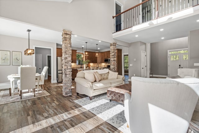 living room featuring a high ceiling, decorative columns, dark wood-type flooring, and sink