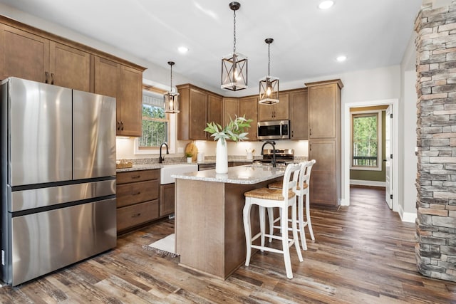 kitchen with sink, dark wood-type flooring, an island with sink, pendant lighting, and appliances with stainless steel finishes