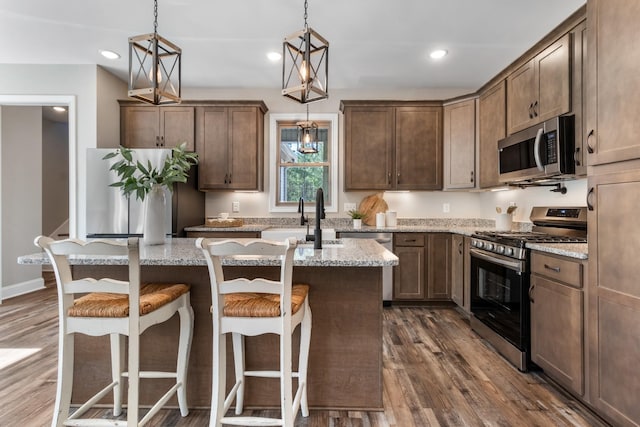 kitchen with light stone counters, pendant lighting, an island with sink, and stainless steel appliances