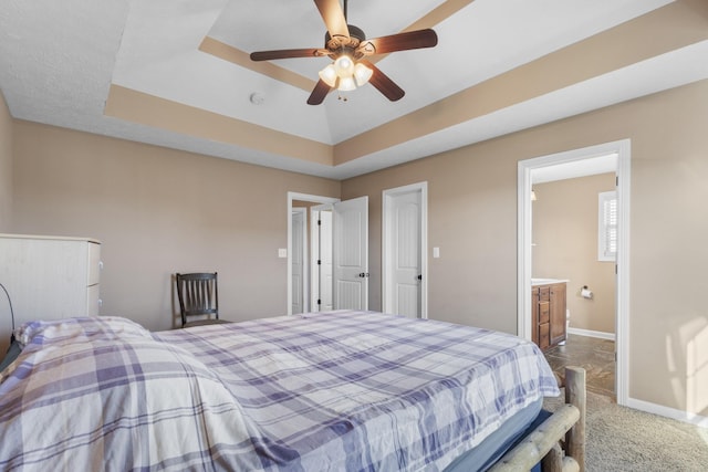 bedroom featuring ceiling fan, carpet floors, a tray ceiling, and ensuite bath