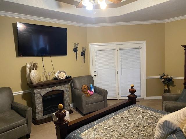 carpeted bedroom featuring ceiling fan, a raised ceiling, ornamental molding, and a fireplace