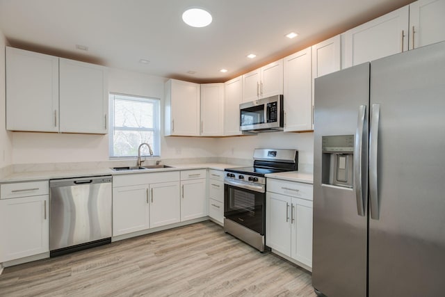 kitchen with sink, white cabinetry, stainless steel appliances, and light wood-type flooring