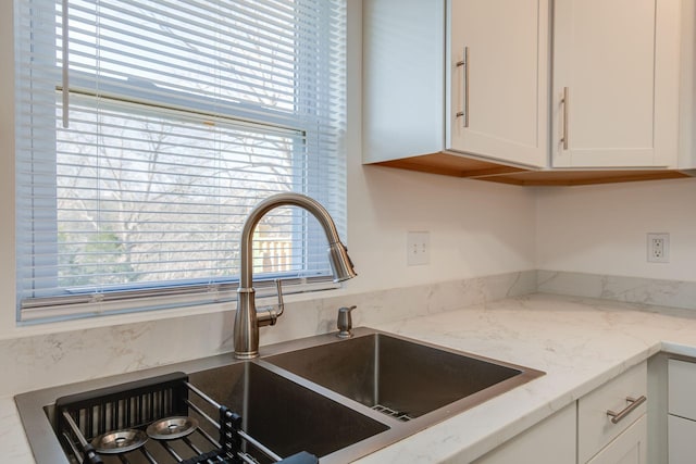 kitchen featuring light stone counters, white cabinetry, and sink