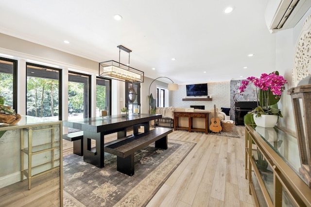 dining area with a wall mounted air conditioner, light wood-type flooring, brick wall, and a brick fireplace