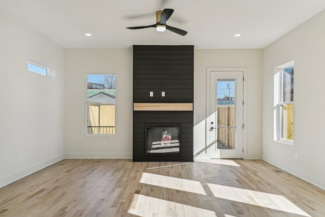 unfurnished living room featuring a large fireplace, ceiling fan, and light hardwood / wood-style flooring