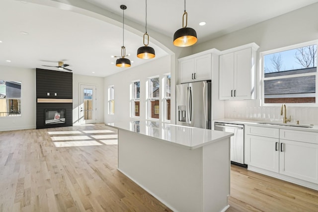 kitchen featuring pendant lighting, white cabinets, sink, a fireplace, and appliances with stainless steel finishes