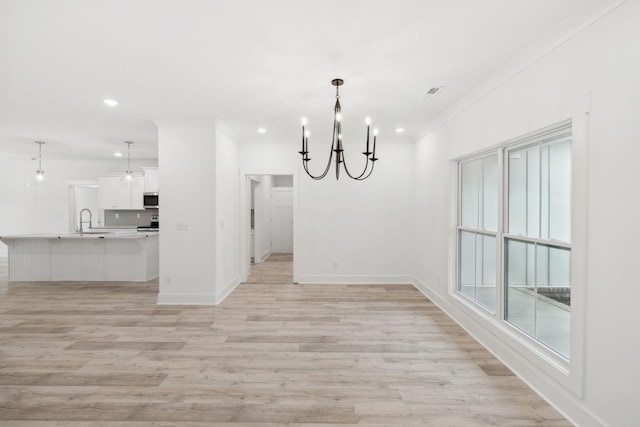 unfurnished dining area featuring a chandelier, ornamental molding, sink, and light hardwood / wood-style flooring