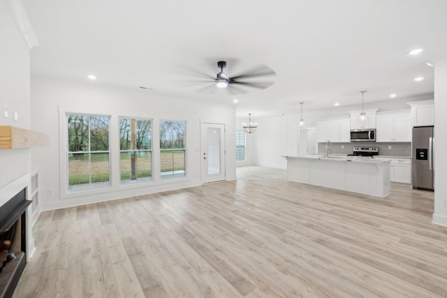 unfurnished living room featuring ceiling fan with notable chandelier, light hardwood / wood-style floors, and crown molding