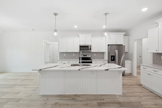 kitchen featuring appliances with stainless steel finishes, light hardwood / wood-style flooring, hanging light fixtures, and an island with sink