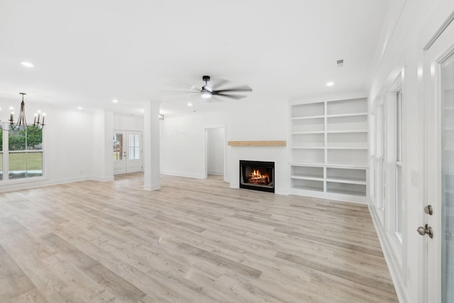 unfurnished living room with built in features, ceiling fan with notable chandelier, and light wood-type flooring