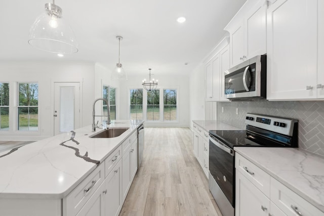 kitchen with stainless steel appliances, sink, decorative light fixtures, white cabinets, and light hardwood / wood-style floors