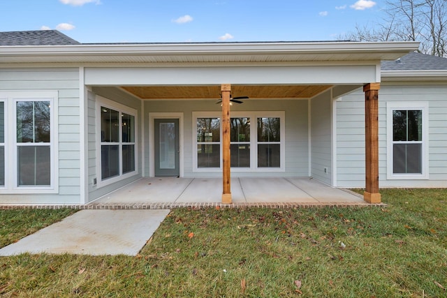 view of exterior entry with ceiling fan, a patio area, and a lawn