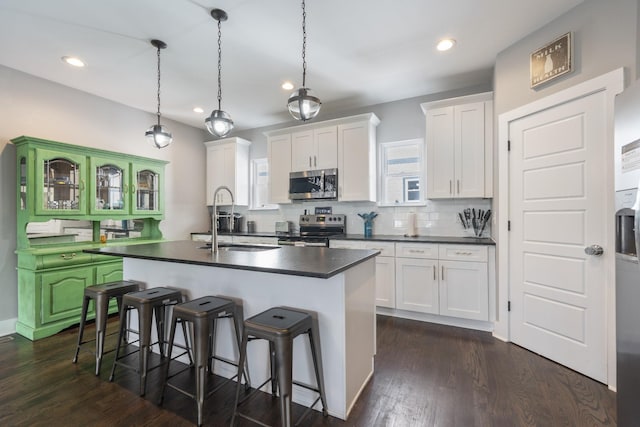 kitchen featuring appliances with stainless steel finishes, pendant lighting, a center island with sink, white cabinets, and dark hardwood / wood-style floors