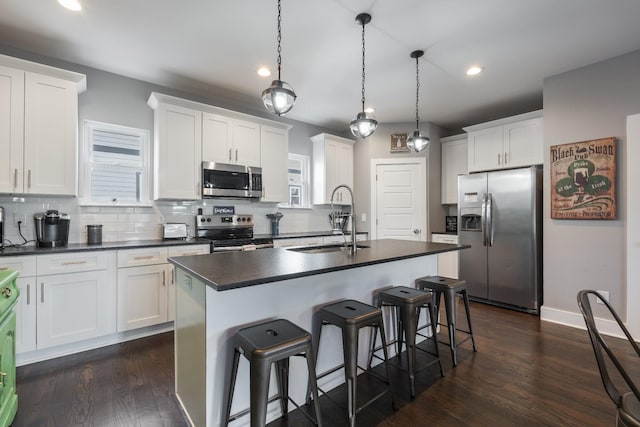 kitchen with appliances with stainless steel finishes, sink, pendant lighting, white cabinetry, and an island with sink