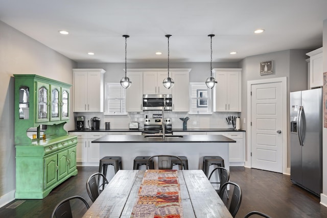 kitchen featuring white cabinetry, a center island with sink, stainless steel appliances, and decorative light fixtures