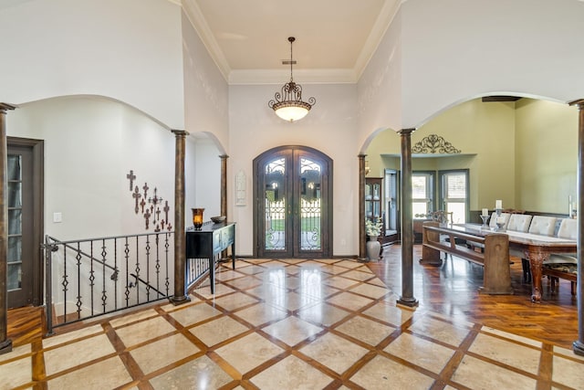 entrance foyer with ornate columns, a towering ceiling, ornamental molding, and french doors