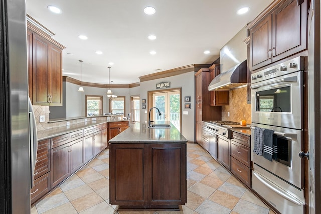 kitchen with decorative backsplash, appliances with stainless steel finishes, sink, decorative light fixtures, and an island with sink