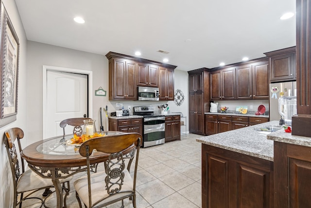 kitchen with dark brown cabinets, light stone counters, light tile patterned floors, and appliances with stainless steel finishes