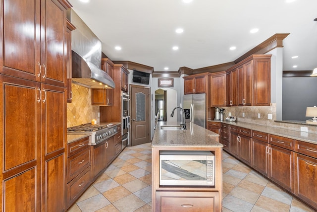 kitchen featuring sink, wall chimney exhaust hood, an island with sink, appliances with stainless steel finishes, and tasteful backsplash