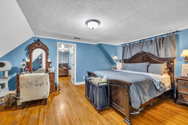 bedroom featuring vaulted ceiling, crown molding, light hardwood / wood-style flooring, and a textured ceiling