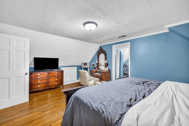 bedroom with a textured ceiling, hardwood / wood-style flooring, and lofted ceiling