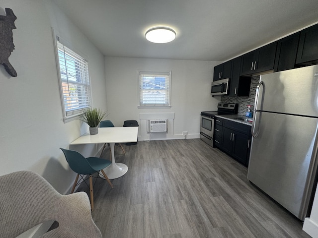 kitchen featuring backsplash, light hardwood / wood-style flooring, a wall unit AC, and appliances with stainless steel finishes