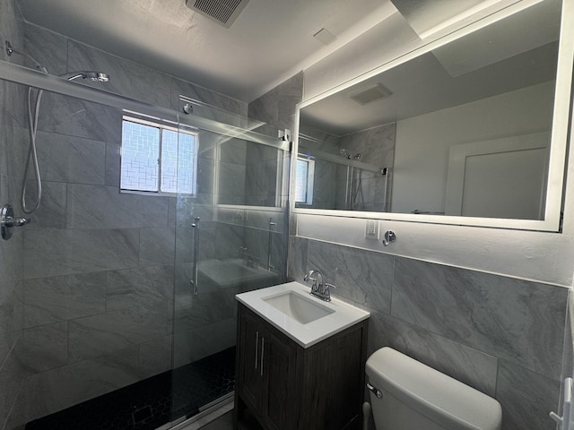 bathroom with vanity, toilet, a shower with shower door, and tile walls