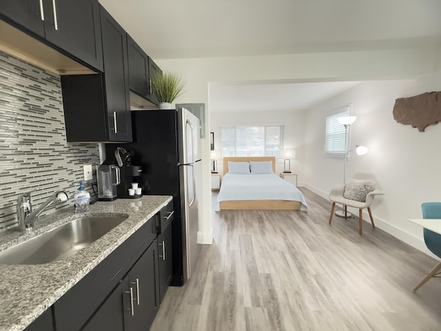 kitchen with light stone countertops, sink, light hardwood / wood-style flooring, and backsplash