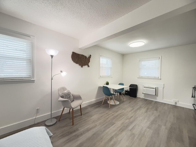 sitting room with hardwood / wood-style flooring, an AC wall unit, a textured ceiling, and beam ceiling