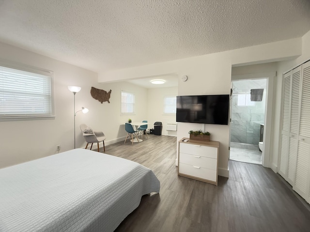 bedroom featuring hardwood / wood-style flooring, ensuite bathroom, a textured ceiling, and multiple windows