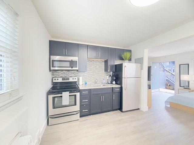 kitchen featuring sink, tasteful backsplash, baseboard heating, appliances with stainless steel finishes, and light hardwood / wood-style floors