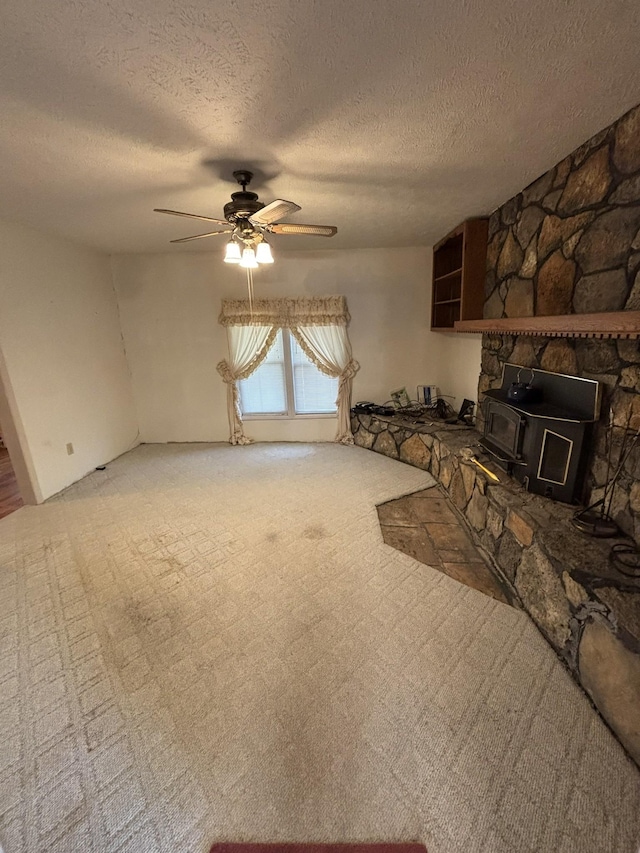 unfurnished living room with carpet, a wood stove, a textured ceiling, and ceiling fan